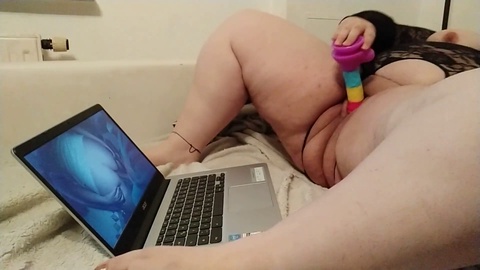 Mollige Frau kommt mit Regenbogen-Dildo, während sie Pornos schaut
