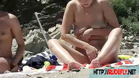 Adolescentes desnudos embadurnándose de aceite en la playa nudista mientras son espiados.
